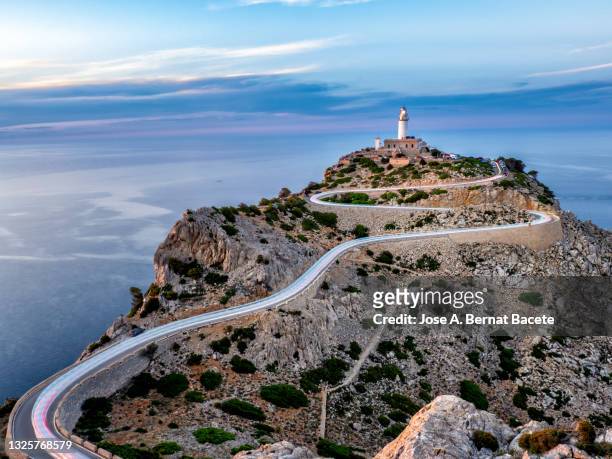 lighthouse on a cliff facing the sea with light trails from cars on the road. majorca island. - cabo formentor stock pictures, royalty-free photos & images