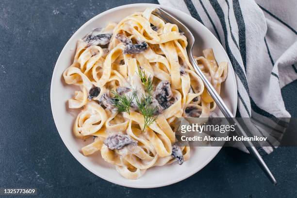 italian pasta fettuccine in a creamy sauce with champignon on a plate, top view - food photography dark background blue stock-fotos und bilder