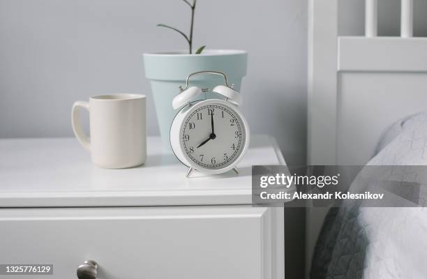 white alarm clock, beige cup with coffee, tea, house plant on bedsite in bedroom. morning concept. - マグカップ ストックフォトと画像