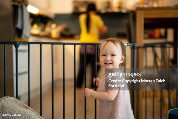 a cheerful baby standing by a baby gate - child playpen stock pictures, royalty-free photos & images