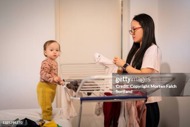 a baby girl tries to help her mom with chores - wäscheständer stock-fotos und bilder
