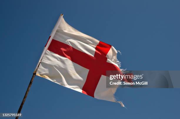 tattered english flag flying in the wind against a clear blue sky - bandiera inglese foto e immagini stock