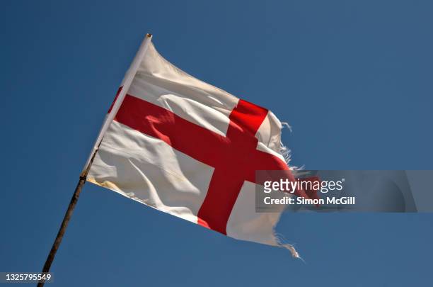 tattered english flag flying in the wind against a clear blue sky - セントジョージ国旗 ストックフォトと画像