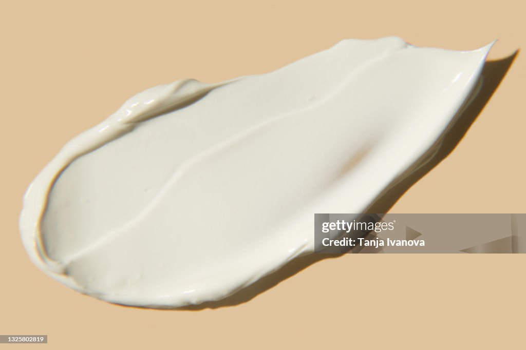 Liquid Textured smear of white cream on beige background. Flat lay, top view, copy space. Cosmetic banner.