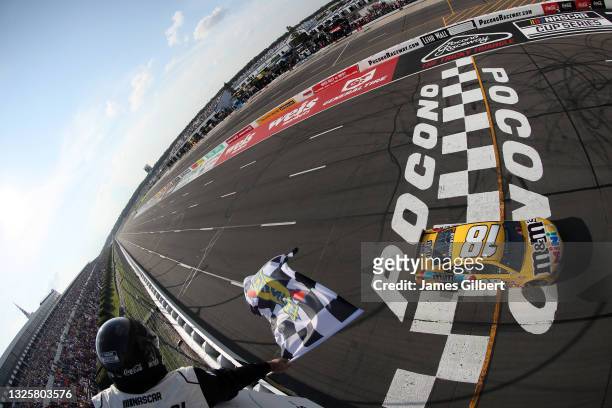 Kyle Busch, driver of the M&M's Mini's Toyota, takes the checkered flag to win the NASCAR Cup Series Explore the Pocono Mountains 350 at Pocono...