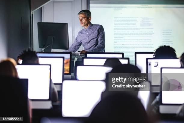 mid adult professor teaching a lecture from desktop pc at computer lab. - computer training stock pictures, royalty-free photos & images