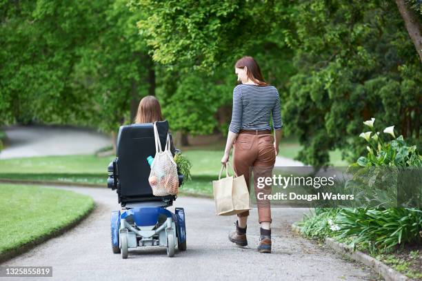 disabled woman and friend with shopping in park. - lichamelijke beperking stockfoto's en -beelden