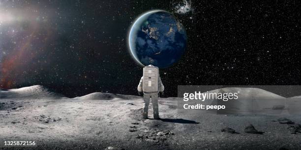 einsamer astronaut im raumanzug steht auf dem mond und schaut auf die ferne erde - textfreiraum stock-fotos und bilder