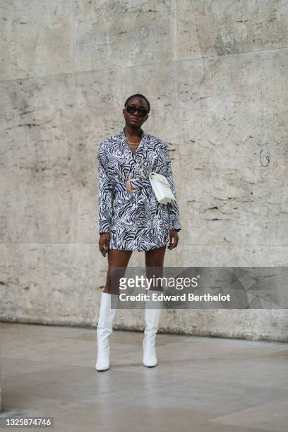 Guest wears sunglasses, a white quilted bag with pearls, a long oversized blazer jacket with black and white zebra printed patterns worn as a dress,...