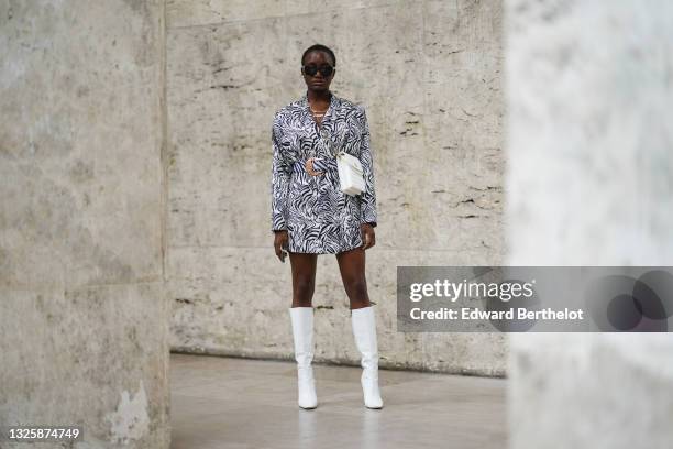 Guest wears sunglasses, a white quilted bag with pearls, a long oversized blazer jacket with black and white zebra printed patterns worn as a dress,...