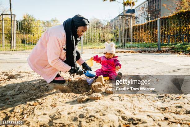 mother playing in sand pit with toddler at the park - sandbox stock-fotos und bilder