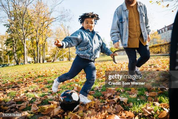 young boy kicking ball while playing soccer with his dad - blue hose soccer stock-fotos und bilder