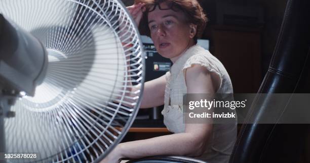 la mujer está tratando de trabajar en la computadora de escritorio en casa, sufriendo de clima caliente y usando ventilador eléctrico - hot older women fotografías e imágenes de stock