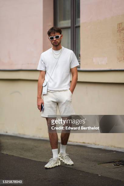 Guest wears white Versace sunglasses, a white t-shirt, white ribbed shorts, a white shiny leather small crossbody bag, a pearls necklace, a gold...
