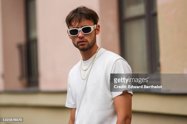 Guest wears white Versace sunglasses, a white t-shirt, white ribbed shorts, a white shiny leather small crossbody bag, a pearls necklace, a gold...