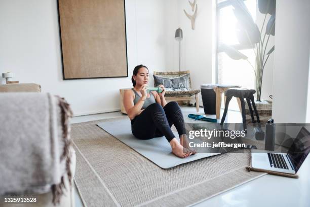 shot of a young woman working out with weights and a laptop at home - sit ups stockfoto's en -beelden