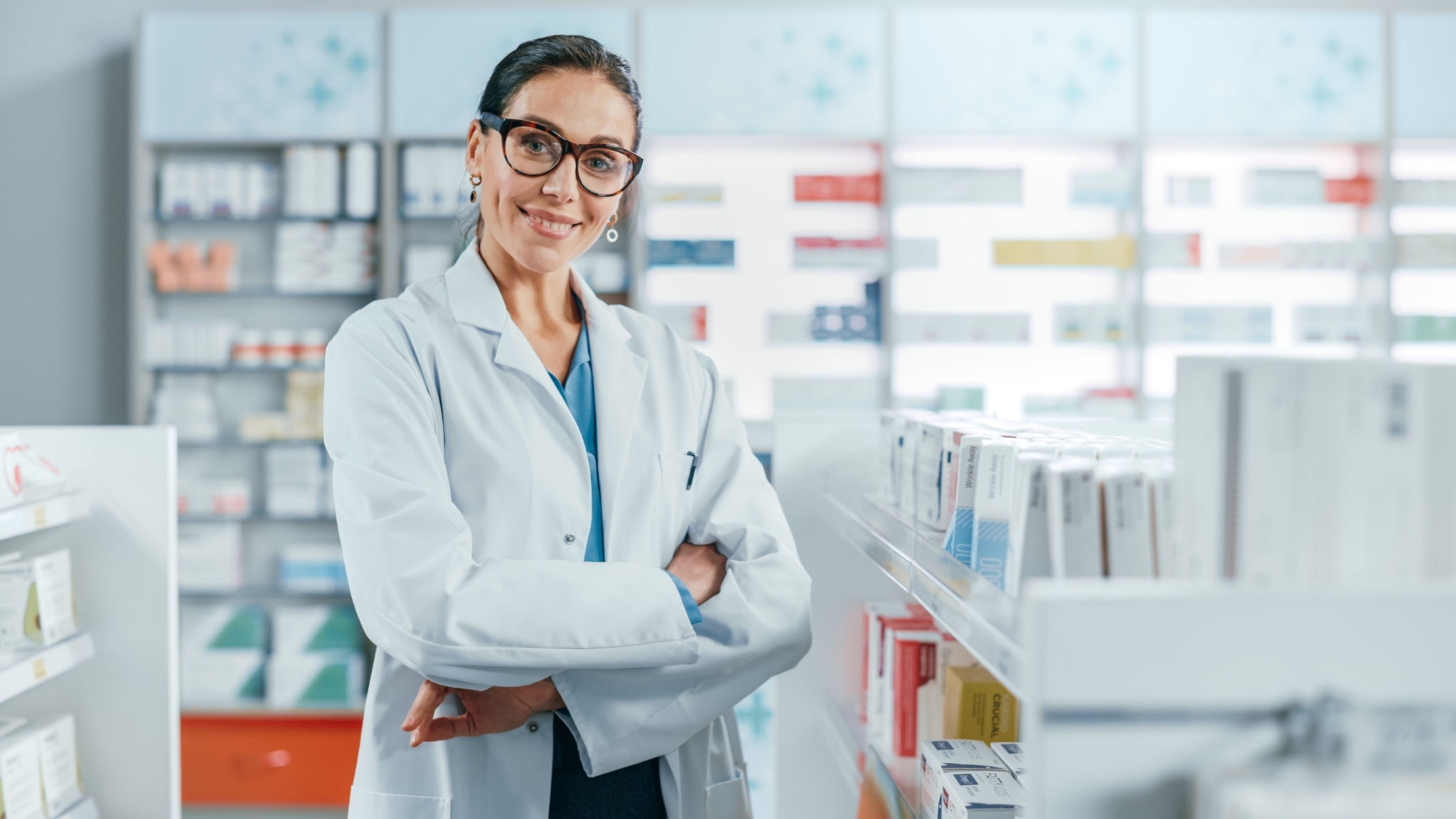 Pharmacy: Portrait of Beautiful Professional Caucasian Female Pharmacist Wearing Glasses, Crosses Arms and Looks at Camera Smiling Charmingly. Drugstore Store with Shelves Health Care Products Pharmacy: Portrait of Beautiful Professional Caucasian Female Pharmacist Wearing Glasses, Crosses Arms and Looks at Camera Smiling Charmingly. Drugstore Store with Shelves Health Care Products