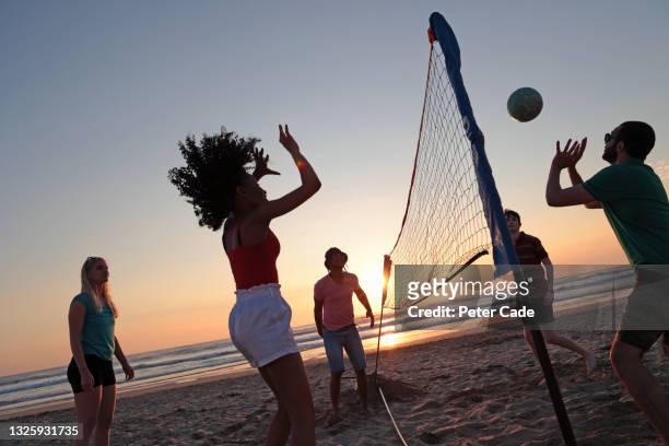group of friends playing volleyball on beach at sunset - beach volleyball group stock pictures, royalty-free photos & images