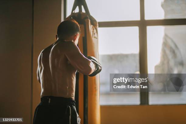 rear view extreme sport asian male muay thai boxer punching sandbag in health club - muaythai boxing stock pictures, royalty-free photos & images