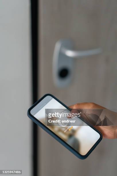 woman locking the door of her house using an app on her cell phone - phone lock stock pictures, royalty-free photos & images