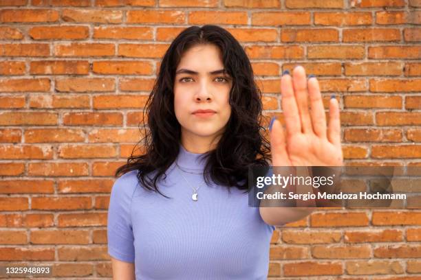 young latino woman looking at the camera and gesturing to stop - brick wall background - 搾取 ストックフォトと画像