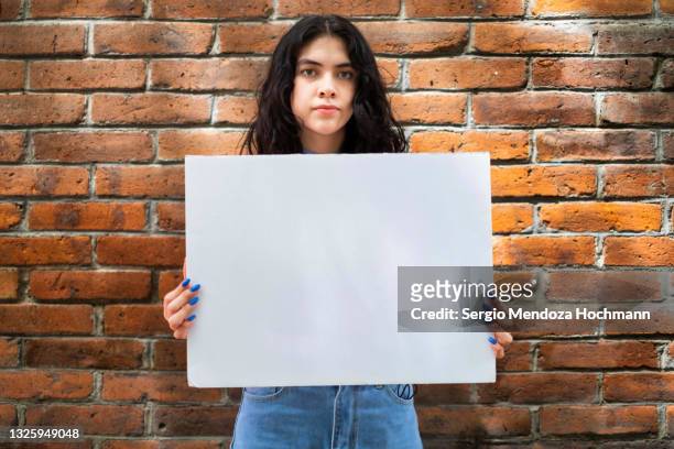 young latino woman holding a blank sign - brick wall background - person holding blank sign fotografías e imágenes de stock