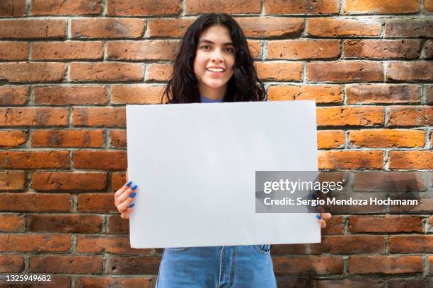 young latino woman smiling and holding a blank sign - brick wall background - women only holding placards stock-fotos und bilder