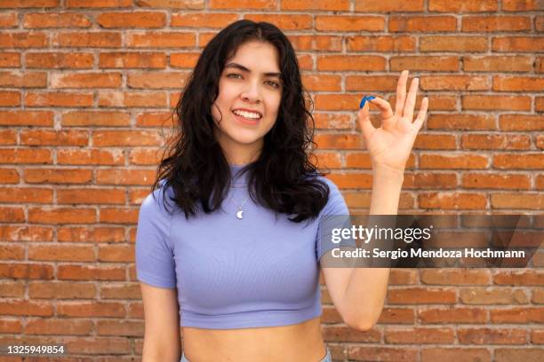 young latino woman smiling, looking at the camera and giving the ok sign - brick wall background - geste de la main photos et images de collection