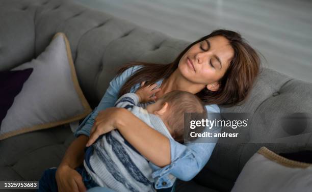 exhausted mother sleeping in the sofa whole holding her baby - mom resting stock pictures, royalty-free photos & images