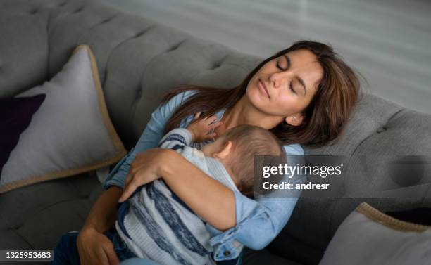 exhausted mother sleeping in the sofa whole holding her baby - mother sleeping baby bildbanksfoton och bilder