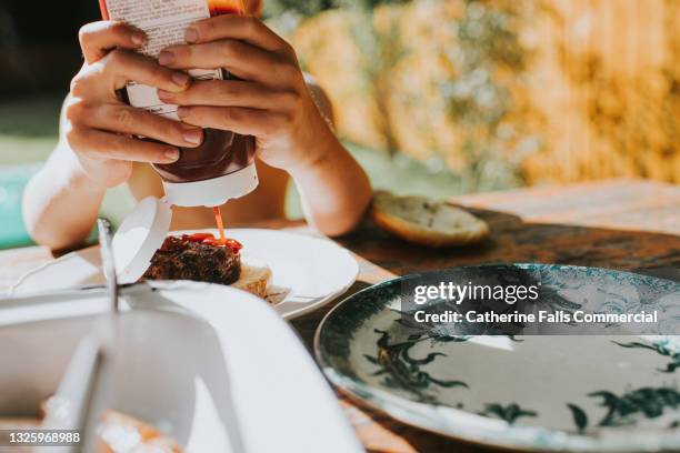 child squeezes tomato ketchup onto a burger - quetschen stock-fotos und bilder