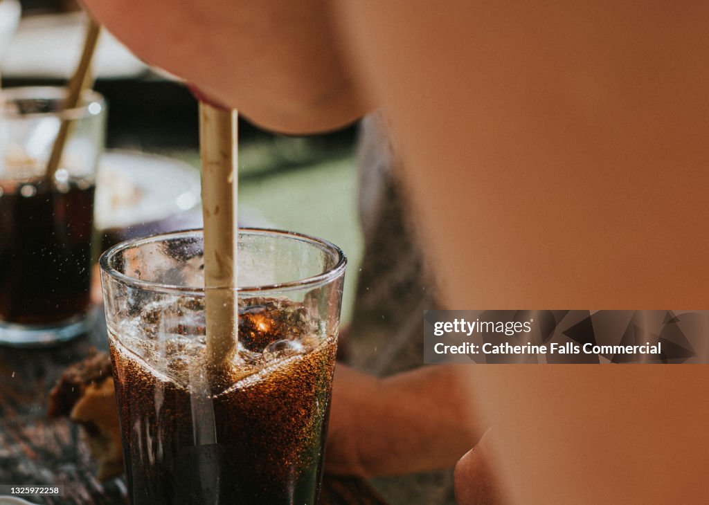 Child drinks fizzy cola juice with a bamboo straw, while dining outside