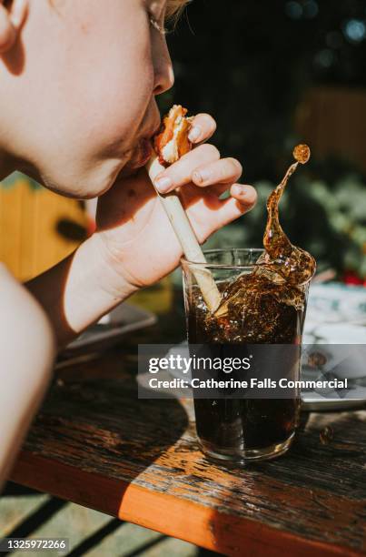 child blows through a bamboo straw, into his carbonated cola drink, creating a splash - cola splash stock pictures, royalty-free photos & images