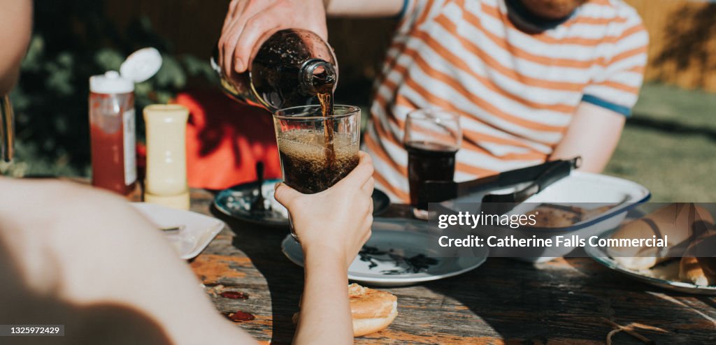 Child holds out a glass as a man pours a carbonated beverage into it