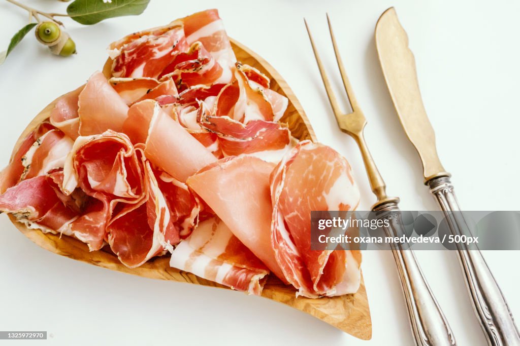 Thin slices of jamon are laid out on a wooden board made of olive wood