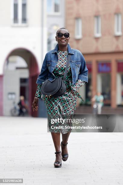 Auma Obama wearing a brown and mint green midi length longsleeve dress with abstract floral pattern and tied waist by Odeeh, a blue denim jeans...