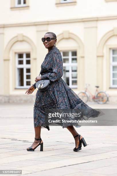 Auma Obama wearing a dark blue midi length longsleeve dress with multicolored abstract pattern, ruffle detail and tied waist by Ulla Johnson, a small...