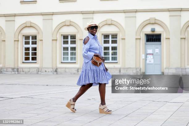 Auma Obama wearing a blue and white striped short cold-shoulder dress with ruffle detail and shoulder cut outs by Talbot Runhof, a small brown bag by...