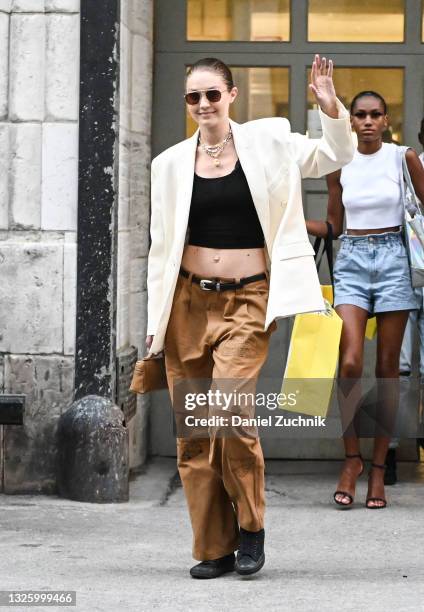 Gigi Hadid is seen wearing a white blazer, black crop top, brown pants and black sneakers outside the Marc Jacobs show on June 28, 2021 in New York...