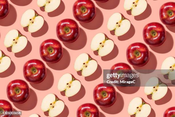 arranged red apples cut in half repetition on light red - apple stockfoto's en -beelden