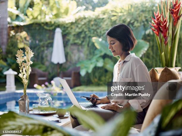 asian woman working from home using laptop, sitting on sofa in open living room - businesswoman couch fotografías e imágenes de stock