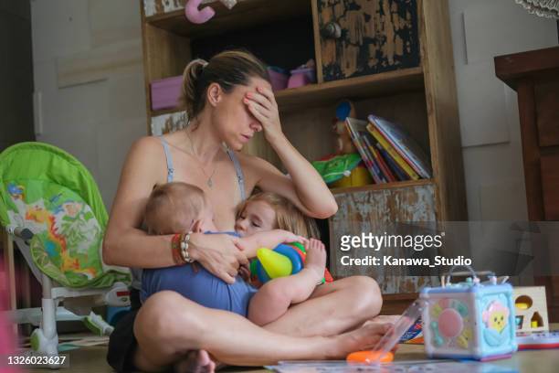 tired mother tandem nursing her two children - mom head in hands stock pictures, royalty-free photos & images