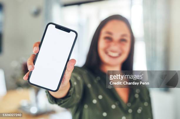 shot of a young businesswoman standing alone in the office and holding her cellphone - display stockfoto's en -beelden