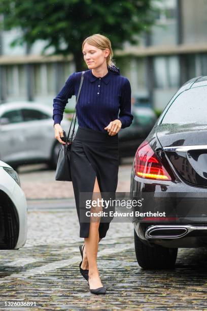 Guest wears a navy blue with white print pattern scarf as a hair elastic, a navy blue ribbed polo shirt, a black shiny leather crossbody bag, a black...