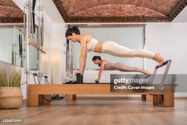 two girls doing the abdominal plank pilates pose over wood reformer - reformer stock pictures, royalty-free photos & images