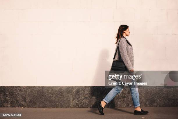 side view of woman walking against wall in city - white handbag stock pictures, royalty-free photos & images