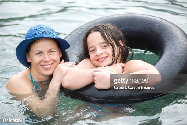 portrait of mother and eleven year-old daughter floating in pool - swimming tube stockfoto's en -beelden
