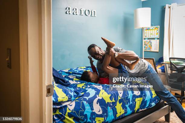 cheerful father playing wrestling with son on bed at home - play fight stock pictures, royalty-free photos & images