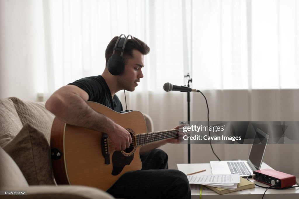 Male songwriter playing guitar on sofa