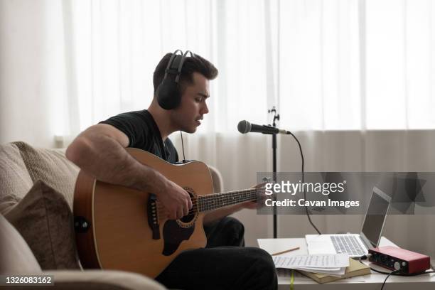 male songwriter playing guitar on sofa - songwriter stock pictures, royalty-free photos & images
